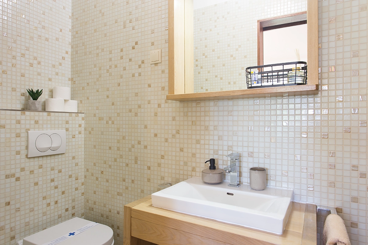 Restroom with a sink, a mirror, and small white tiles.